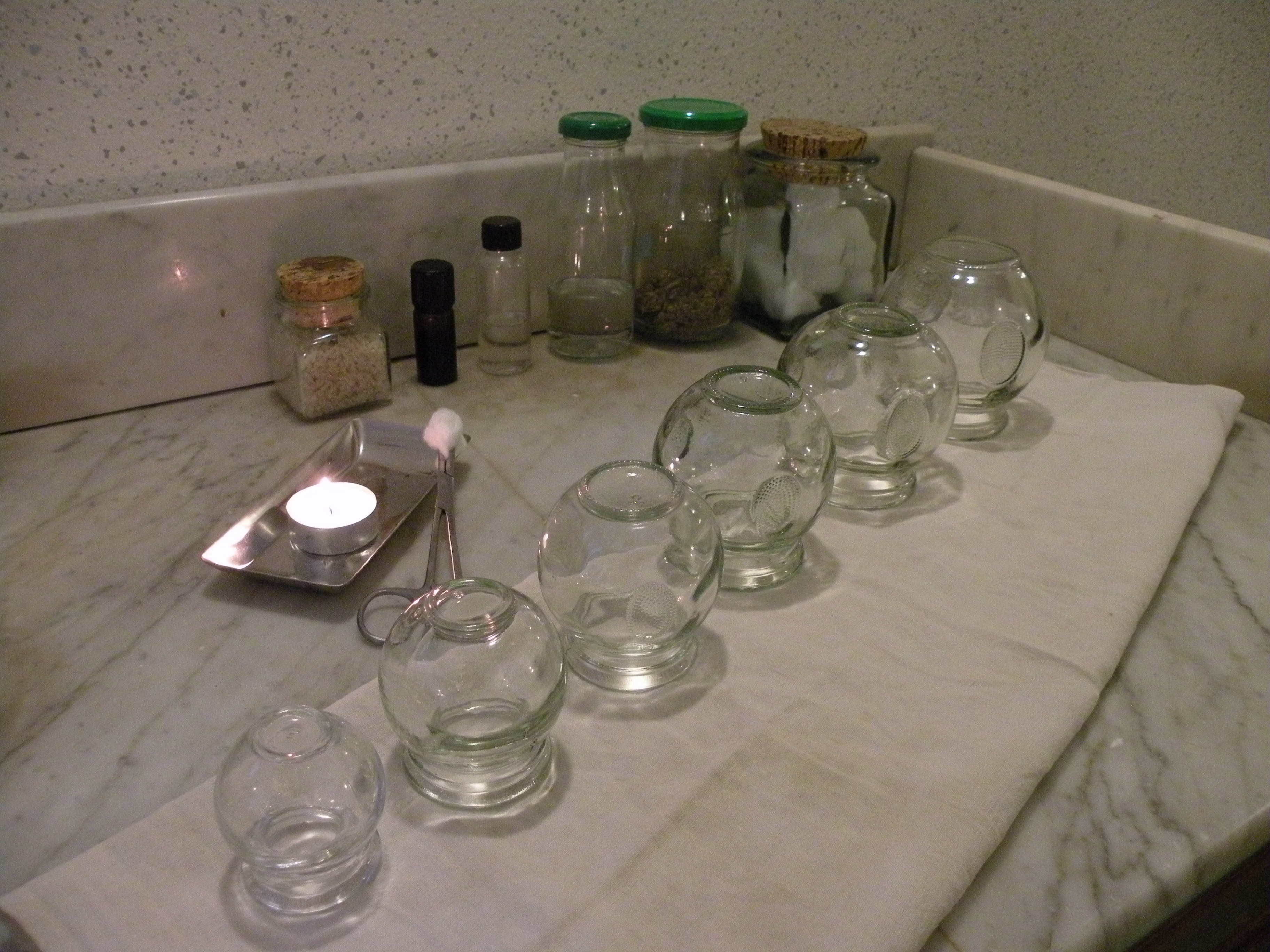 Sur une tablette en marbre, des ventouses alignée avec une boujie allumée. Au fond du petit matériel de soin